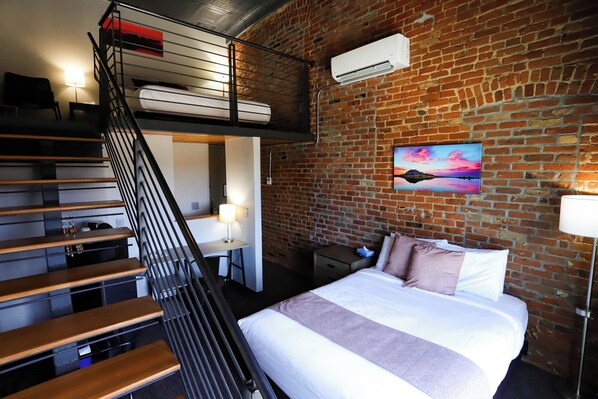 A room with a bunk bed, a desk, a chair, a bed with pillows, and a painting on the wall. - The Hotel Sturgis (Sturgis)