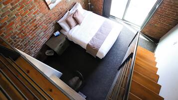 Un dormitorio con pared de ladrillo, una cama con colcha a rayas, una mesita de noche y un ventanal.