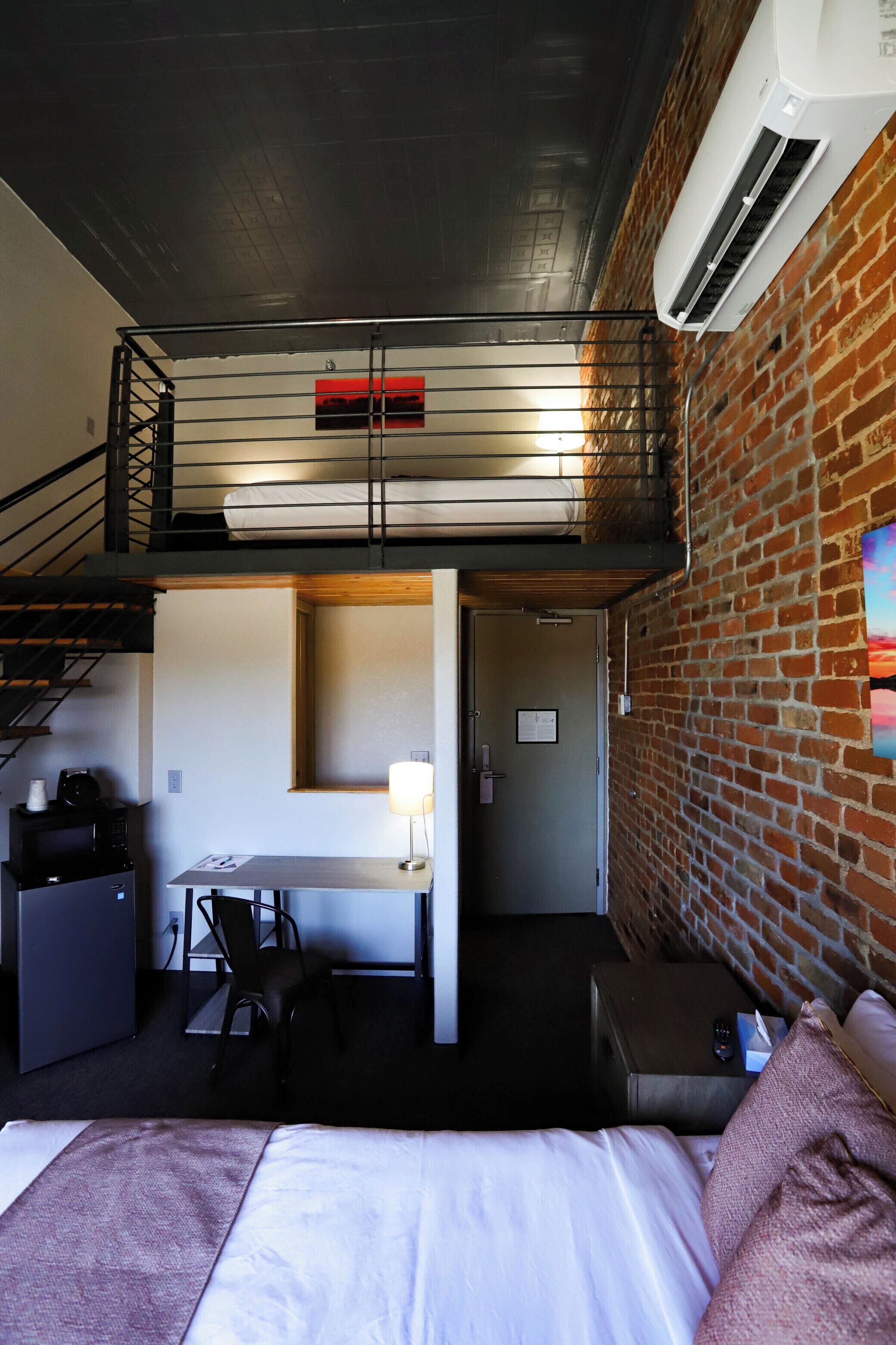 A compact hotel room with a bunk bed, a desk, a chair, a small table, and a bed.