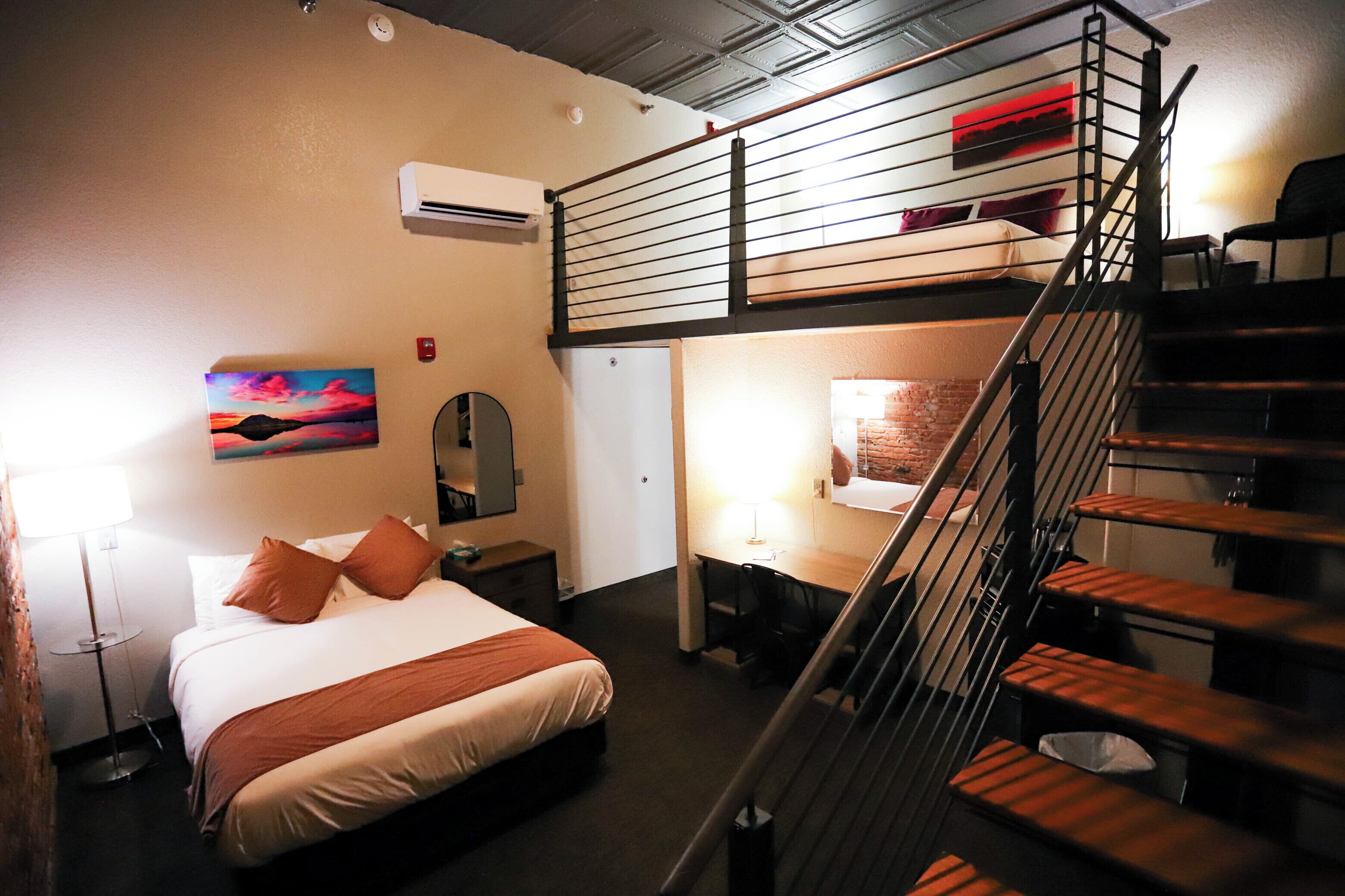 A hotel room with a bed, desk, and a staircase.
