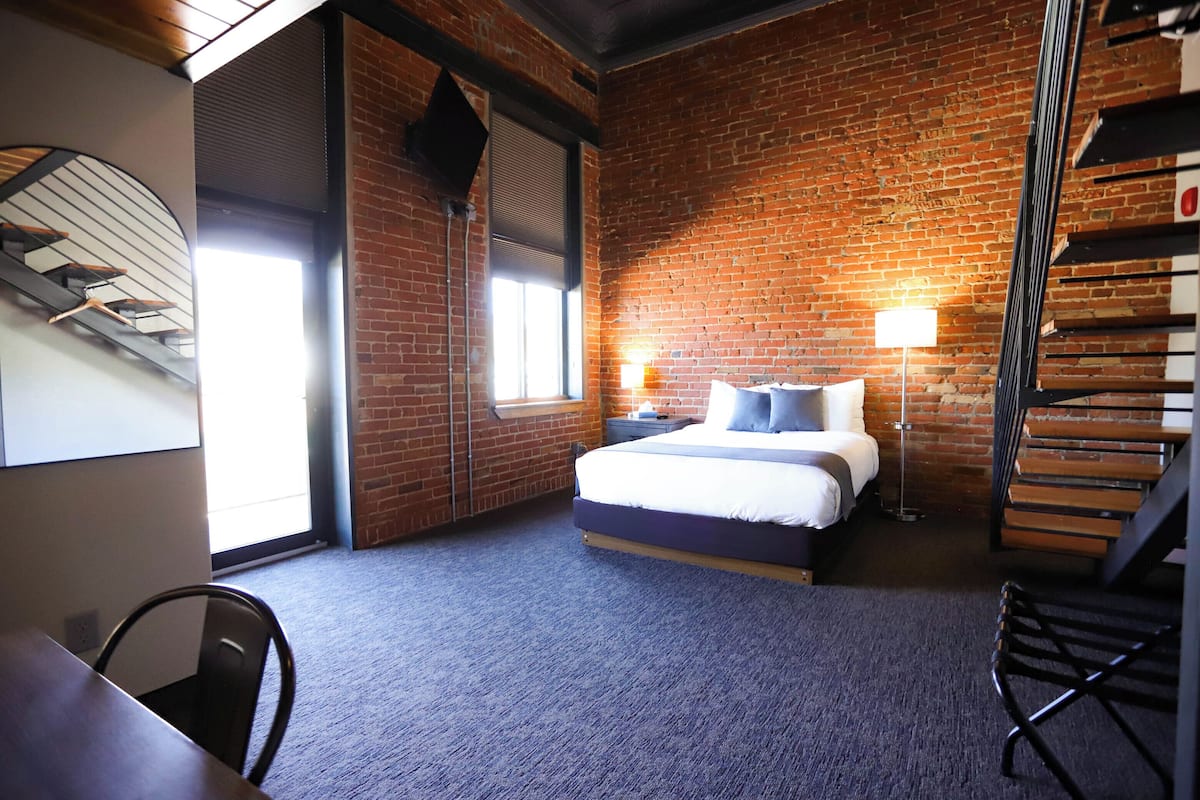 A bedroom with a brick wall, a bed, a desk, and a chair.