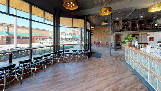A spacious cafe with large windows, wooden flooring, and modern bar stools. - The Hotel Sturgis (Sturgis)
