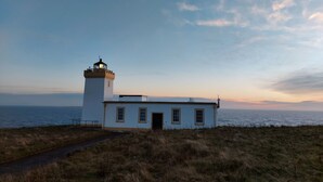 Un faro con un edificio blanco contiguo, con vistas al mar.