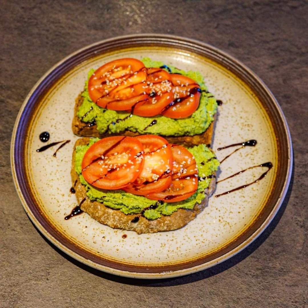 Two slices of avocado toast on a ceramic plate with sesame seeds and a drizzle of sauce.