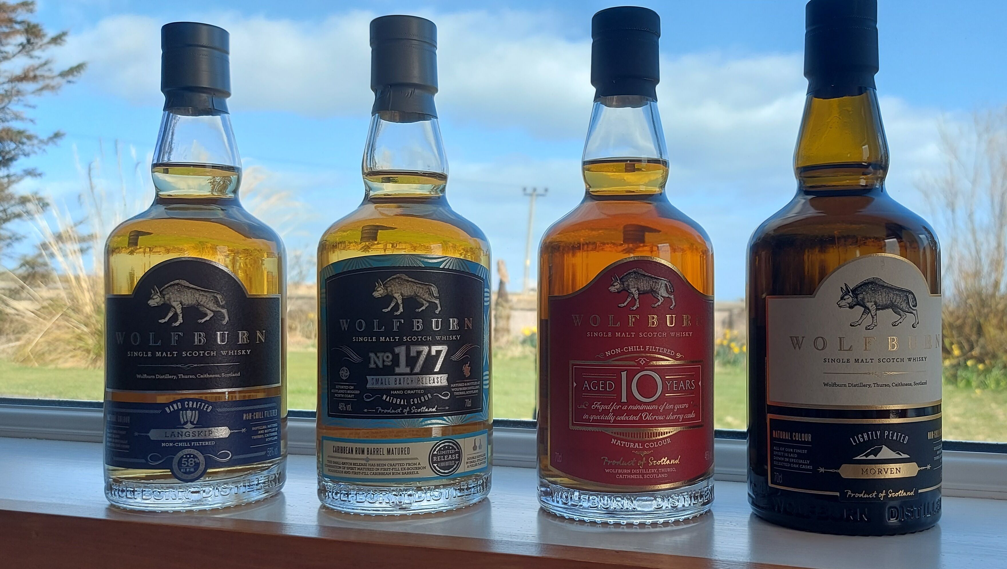 Four bottles of whisky on a windowsill with a scenic view.