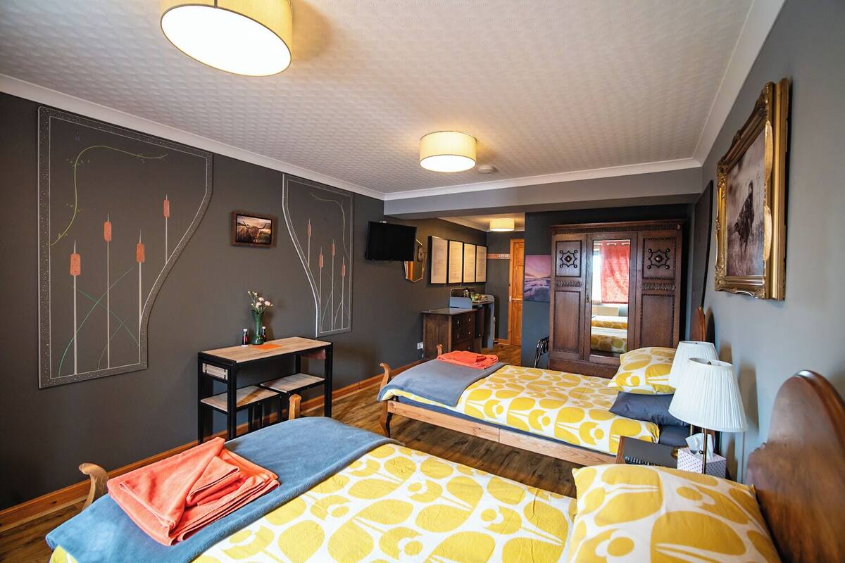 A hotel room with two beds, a desk, a chair, a TV, and a wardrobe.