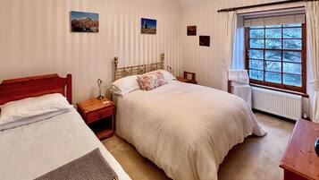 Une chambre avec deux lits simples, une tête de lit en bois, une table de chevet, une lampe de chevet, une fenêtre avec des rideaux et un radiateur.