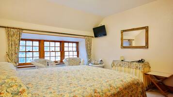 A bedroom with a large bed, two chairs, a television, a mirror, and a window with curtains.