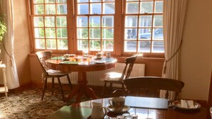 A dining area with a wooden table set for two, a window with curtains, and a patterned carpet. - Scourie Lodge B&B and Gardens (Scourie)