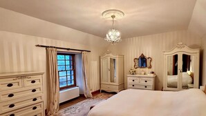 A bedroom with a large bed, a dresser, a mirror, and a window with curtains. - Scourie Lodge B&B and Gardens (Scourie)