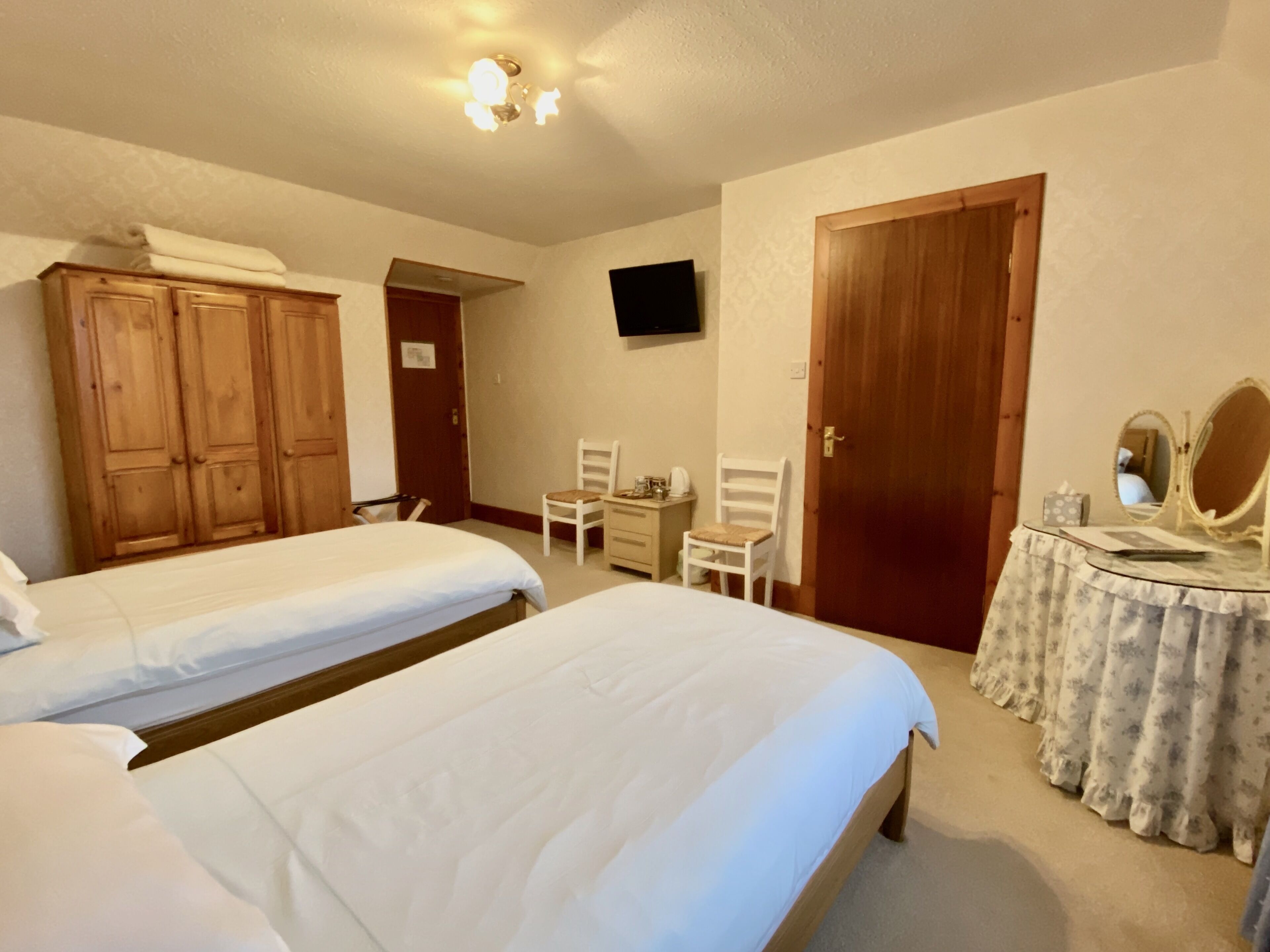 Een hotelkamer met twee bedden, een bureau met spiegel, een stoel en een televisie aan de muur.