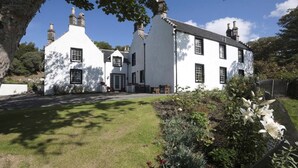 A white building with multiple chimneys, a well-maintained lawn, and flowering plants. - Scourie Lodge B&B and Gardens (Scourie)