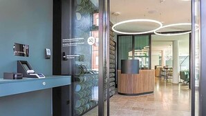A reception area with a glass door, a reception desk, and a modern interior with a circular light fixture. - Art Hotel Ahlen (Ahlen)