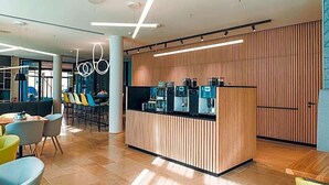 A modern reception area with a wooden panel wall, a coffee station, and seating arrangements. - Art Hotel Ahlen (Ahlen)