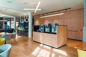 Un espace d’accueil moderne avec un mur revêtu de panneaux en bois, un coin café et des sièges confortables.