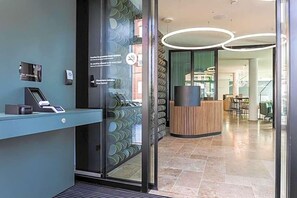 Un espace d’accueil doté d’une porte en verre, d’un comptoir de réception et d’un intérieur moderne agrémenté d’un luminaire circulaire.