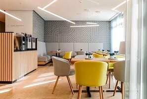 Un intérieur de restaurant moderne avec un comptoir d’accueil, un espace salon et un mur décoré de motifs.