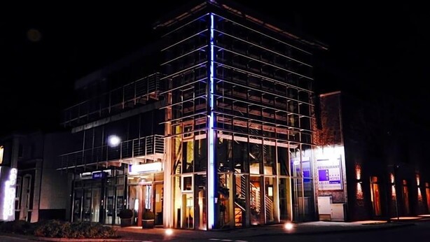 A multi-story building with a glass facade, a visible staircase, and a sign indicating a restaurant and hotel. - Art Hotel Ahlen (Ahlen)