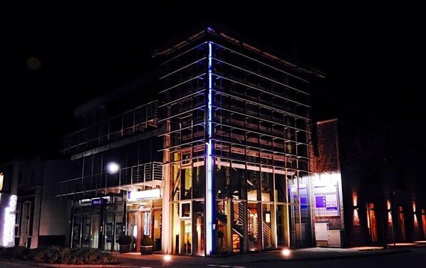 Un immeuble à plusieurs étages doté d’une façade en verre, d’un escalier apparent et d’une enseigne indiquant la présence d’un restaurant et d’un hôtel.