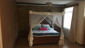 A bedroom with a four-poster bed, wooden flooring, a brick wall, and a window with curtains.