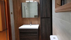 A bathroom with a wooden vanity, a white sink, and a mirror above it.