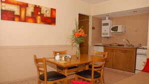 A compact kitchen with a microwave, stove, and sink. There is a dining table with chairs and a vase with flowers. - Concord Rent Apart (Córdoba)