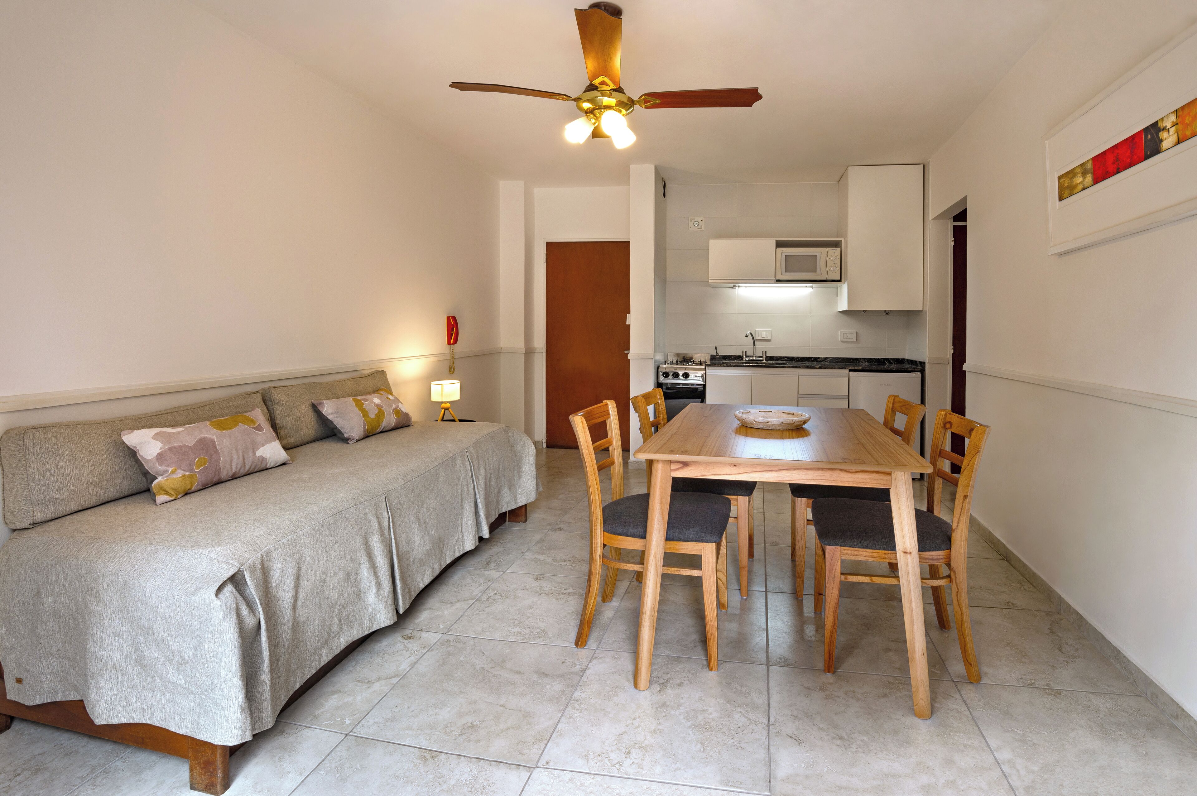 A compact living space with a sofa, dining table, and chairs, a kitchenette, and a ceiling fan.