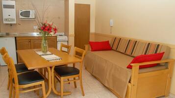 Un espace de vie compact comprenant un coin cuisine, une table à manger avec des chaises et un canapé agrémenté d’un coussin à rayures.