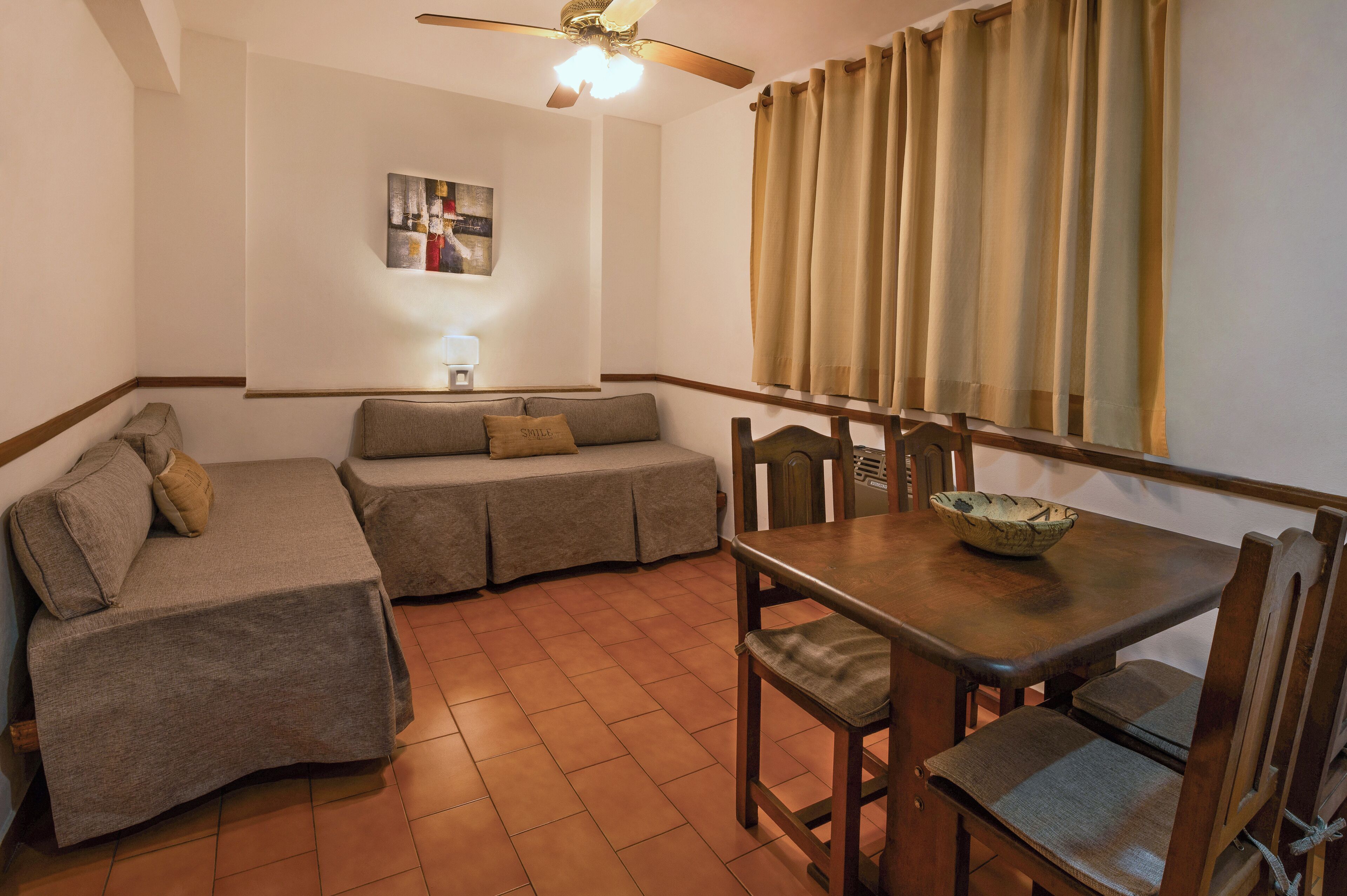 A room with a sofa, a dining table with chairs, a ceiling fan, and a window with curtains.