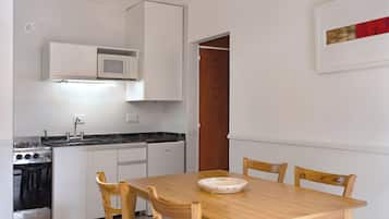 Cuina petita amb armaris blancs, microones, fogó i un rentaplat. Hi ha una taula de dinar amb caires i un plat decoratiu.