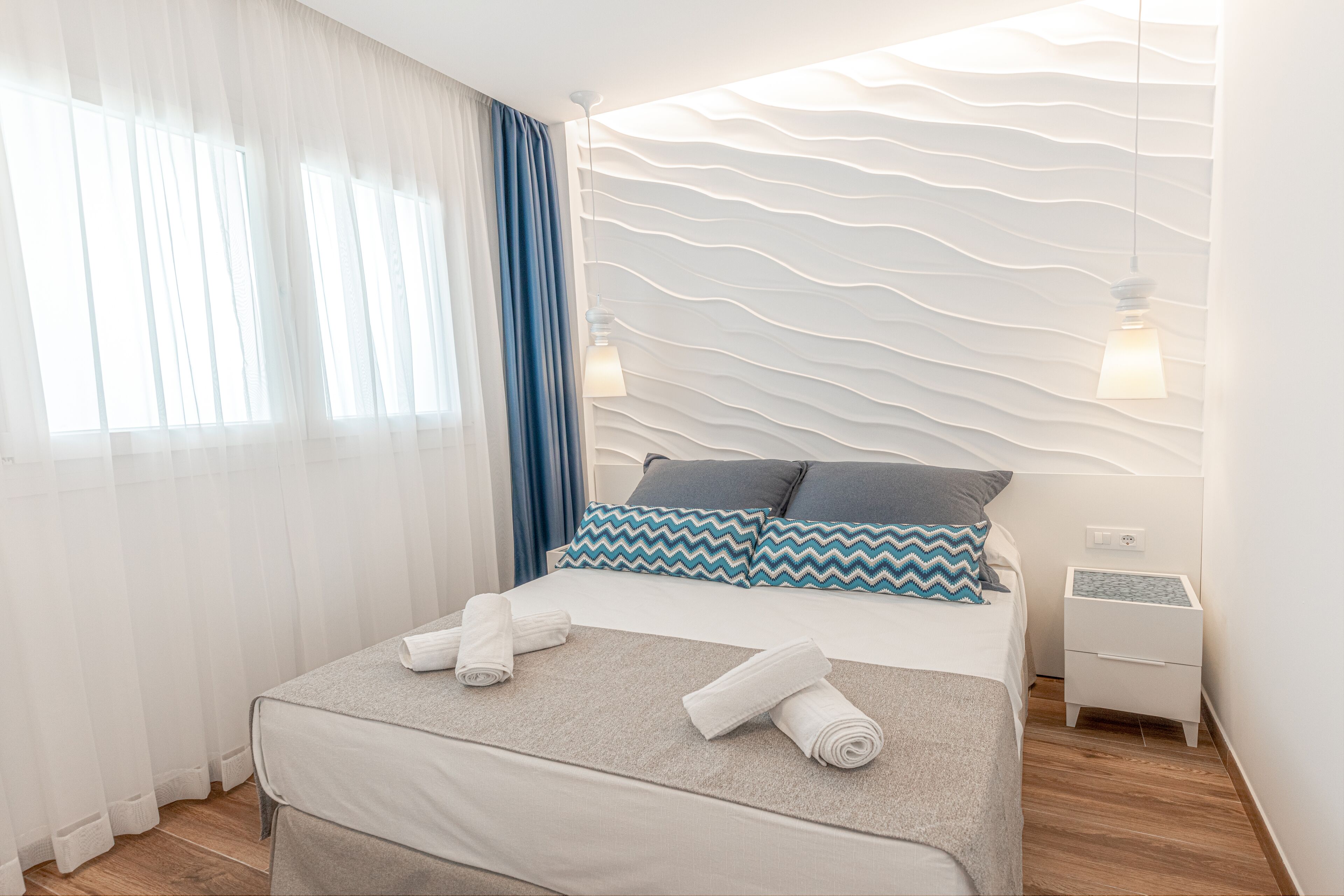 Una habitación de hotel moderna con una cama bien hecha, una mesita de noche y una pared con textura.