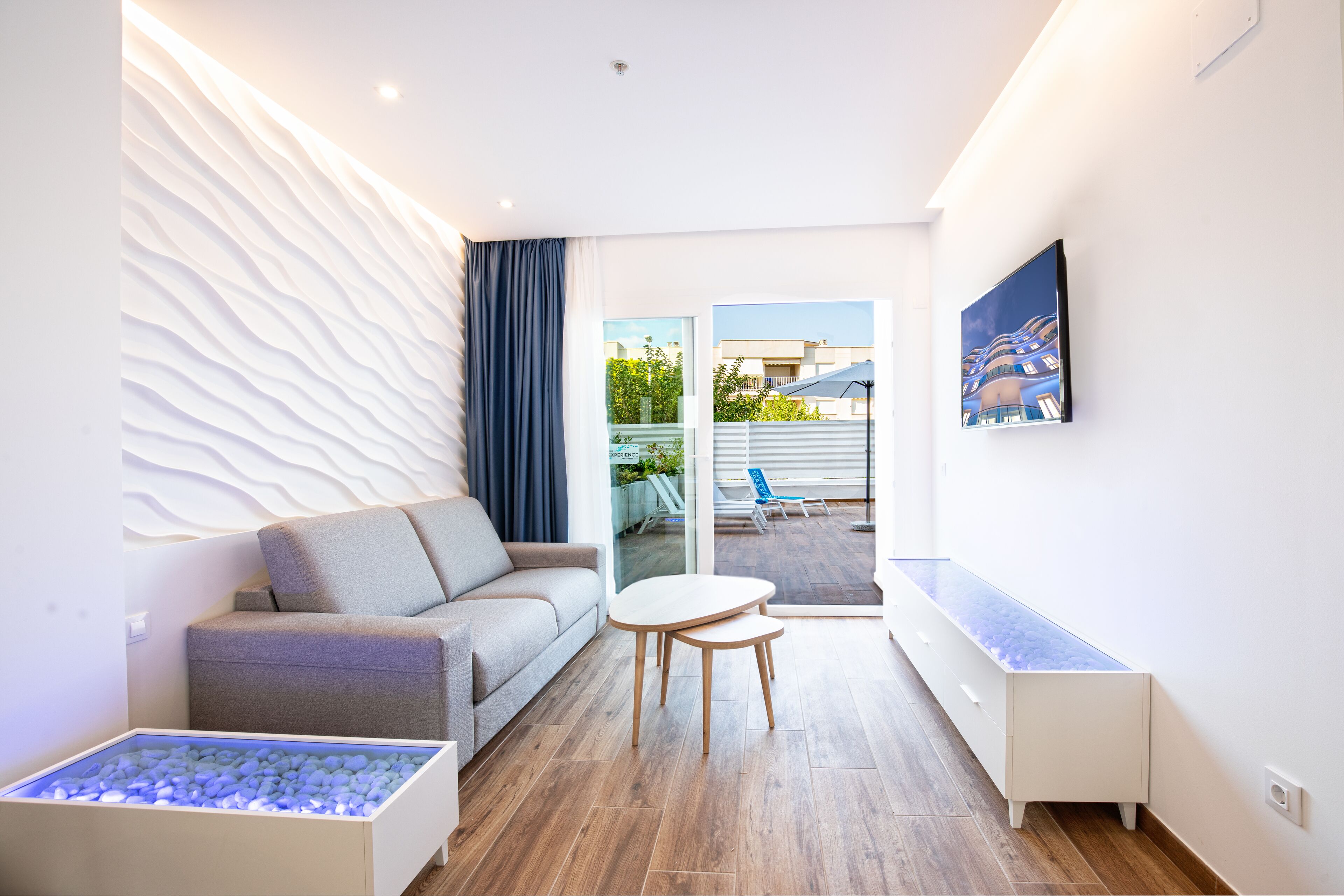 A modern living room with a sofa, a coffee table, a glass-top table, and a built-in aquarium.