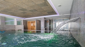 En indendørs swimmingpool med et vandfald, flisebeklædte vægge og en trædør.