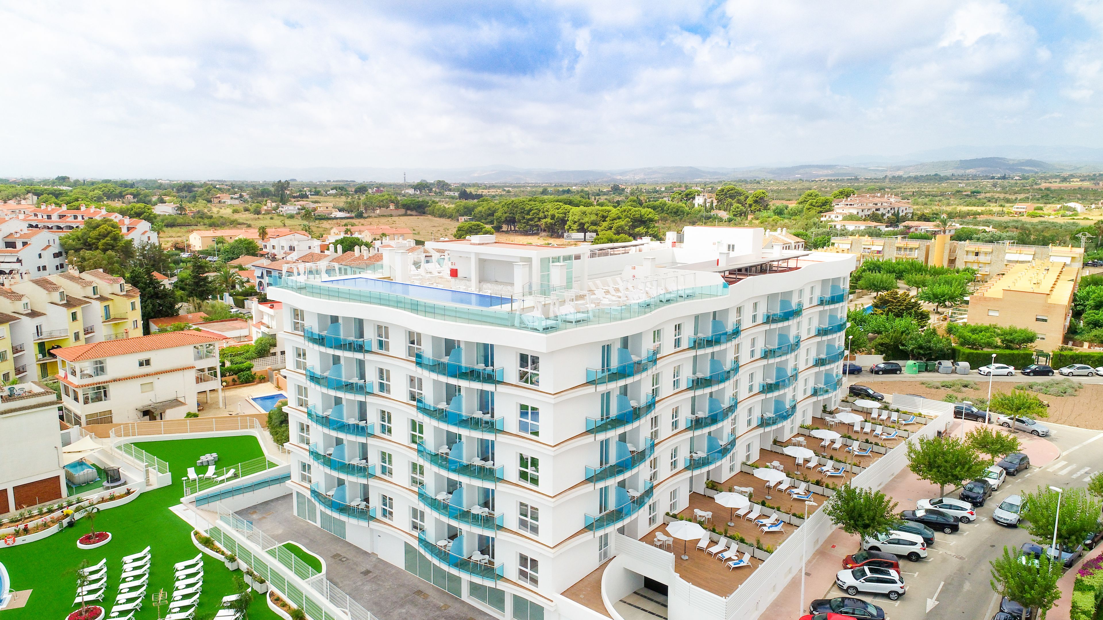 A multi-story hotel with balconies, a rooftop pool, and a view of the surrounding cityscape.