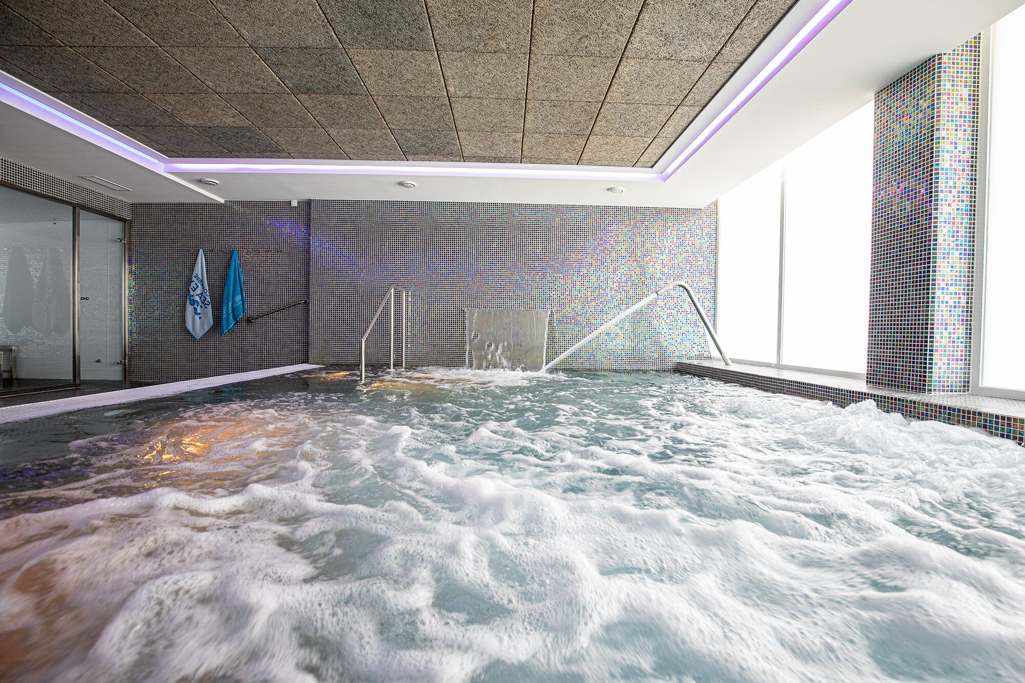 Un cuarto de spa con un amplio jacuzzi, paredes con azulejos y un techo con textura.