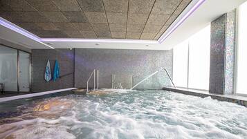 Un cuarto de spa con un amplio jacuzzi, paredes con azulejos y un techo con textura.
