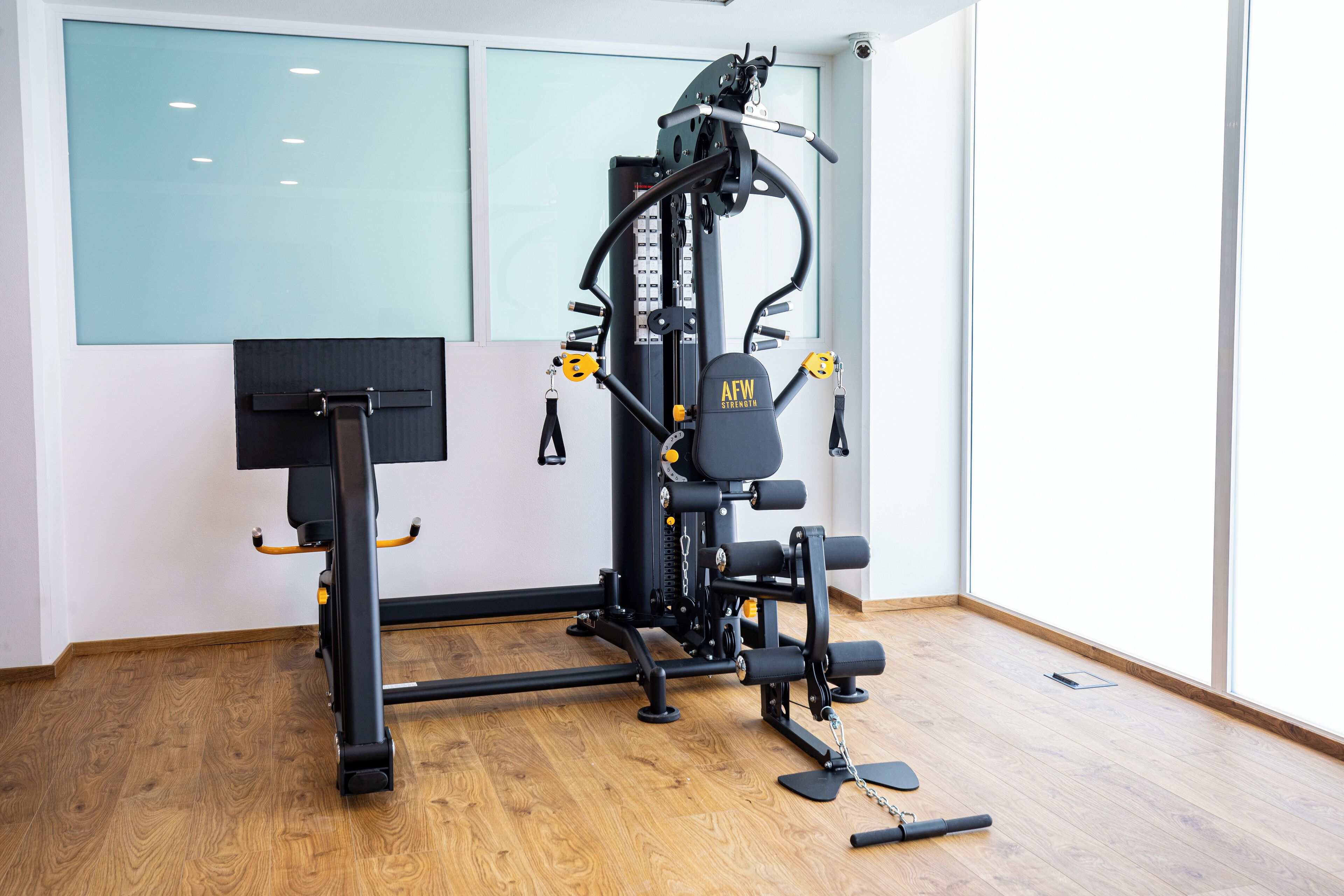 A gym with a multi-functional workout machine, a pull-up bar, and a yoga mat on the floor.
