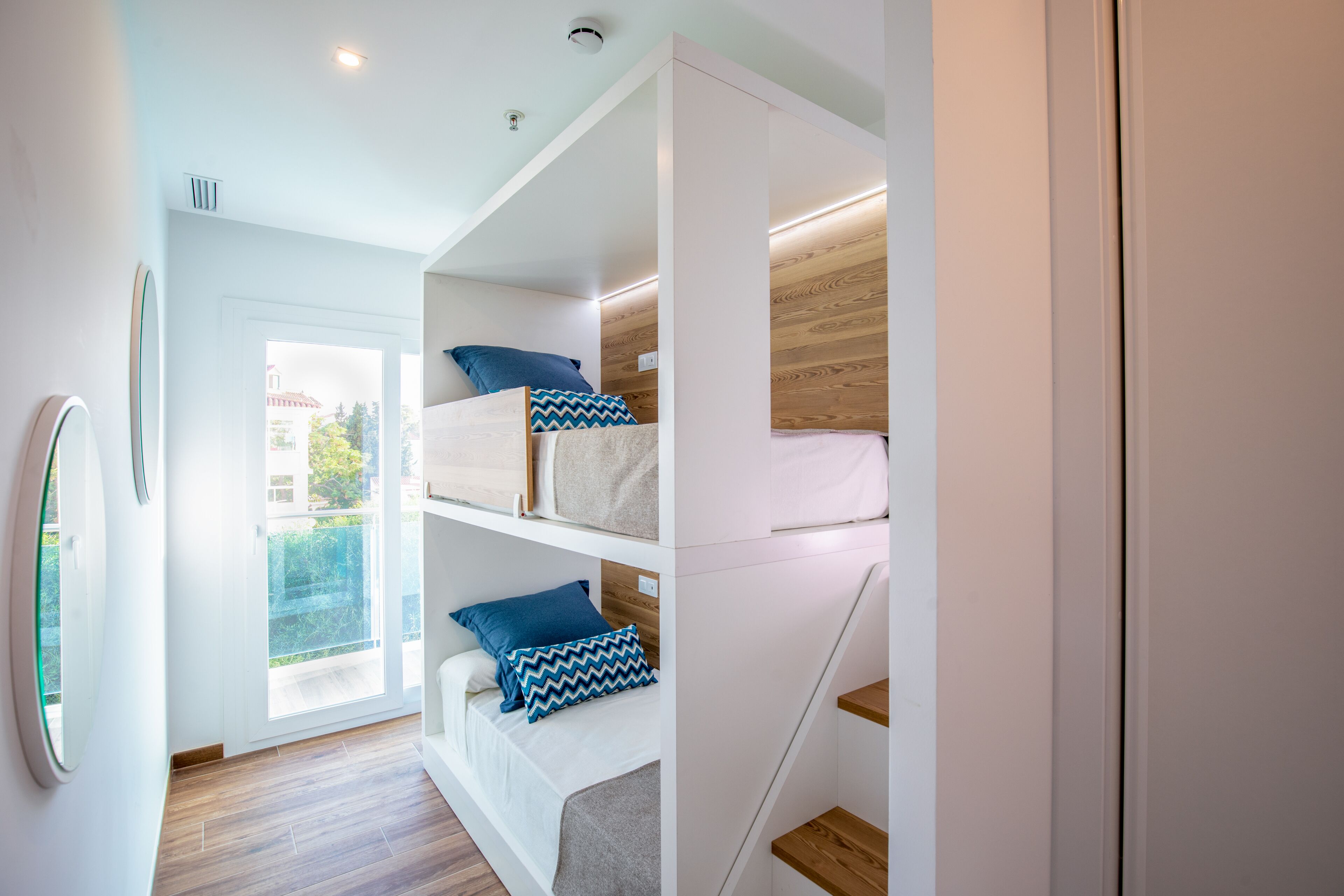 Une chambre moderne avec des lits superposés, une porte coulissante donnant sur un balcon et un plancher en bois.
