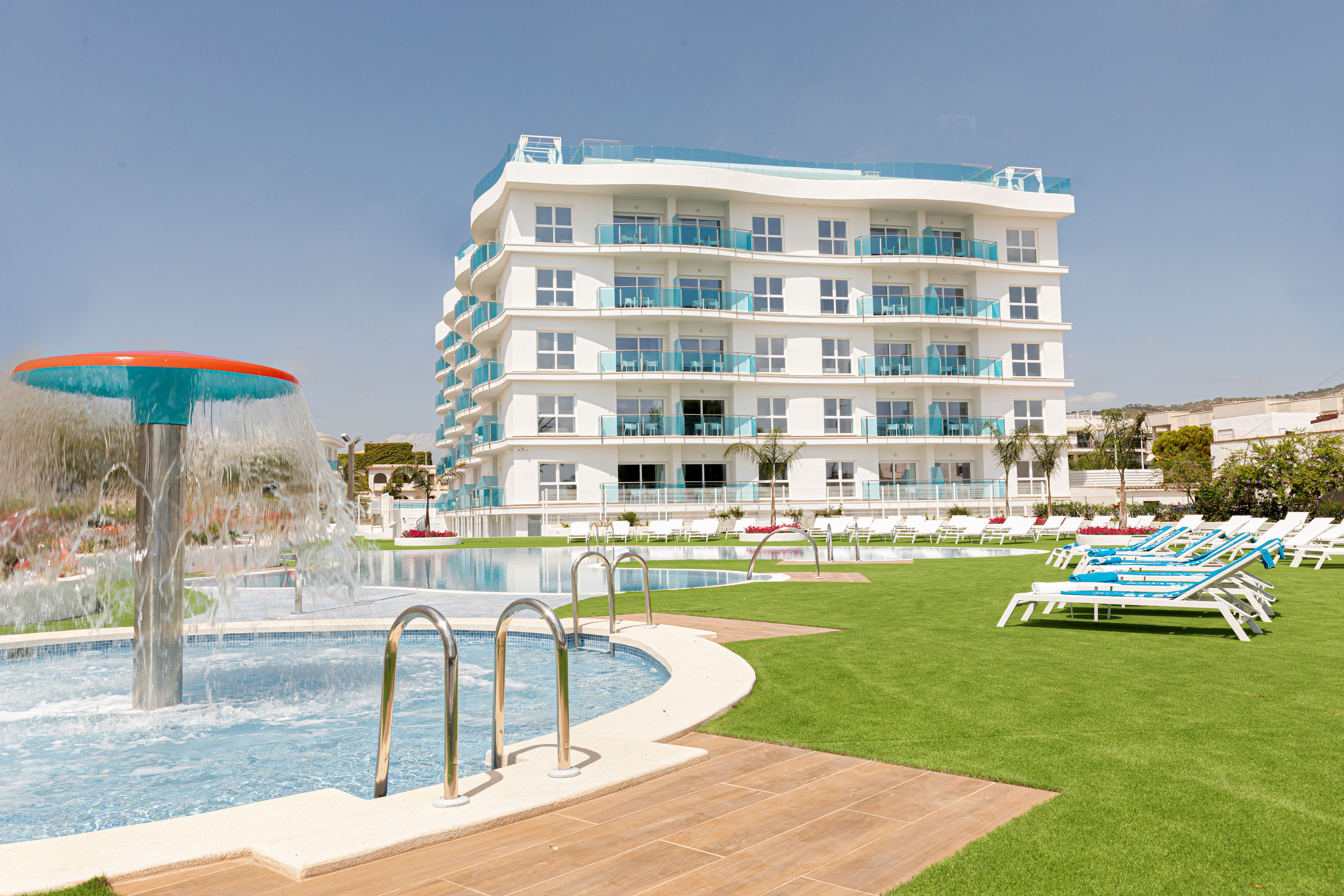 Un hotel con piscina, varios balcones y tumbonas.