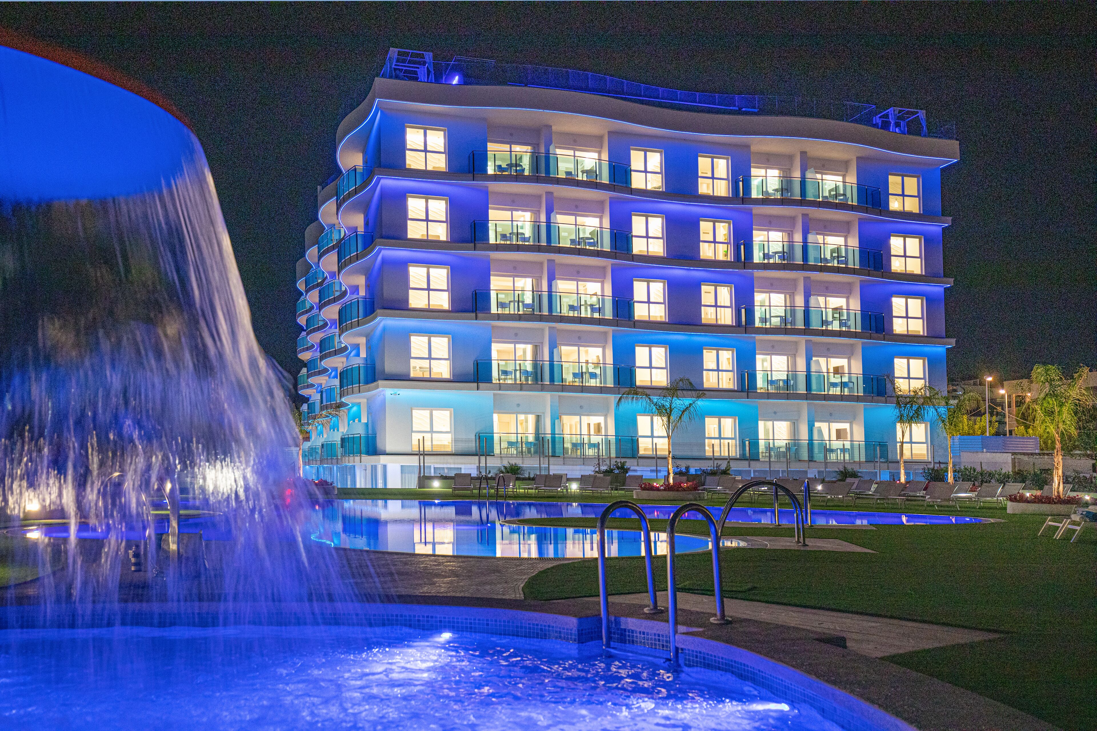 A multi-story hotel with balconies, a swimming pool, and a fountain.
