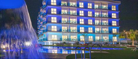 A multi-story hotel with balconies, a swimming pool, and a fountain.