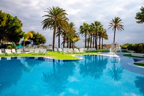 Una piscina de agua cristalina azul, rodeada de palmeras y sillas de descanso blancas.