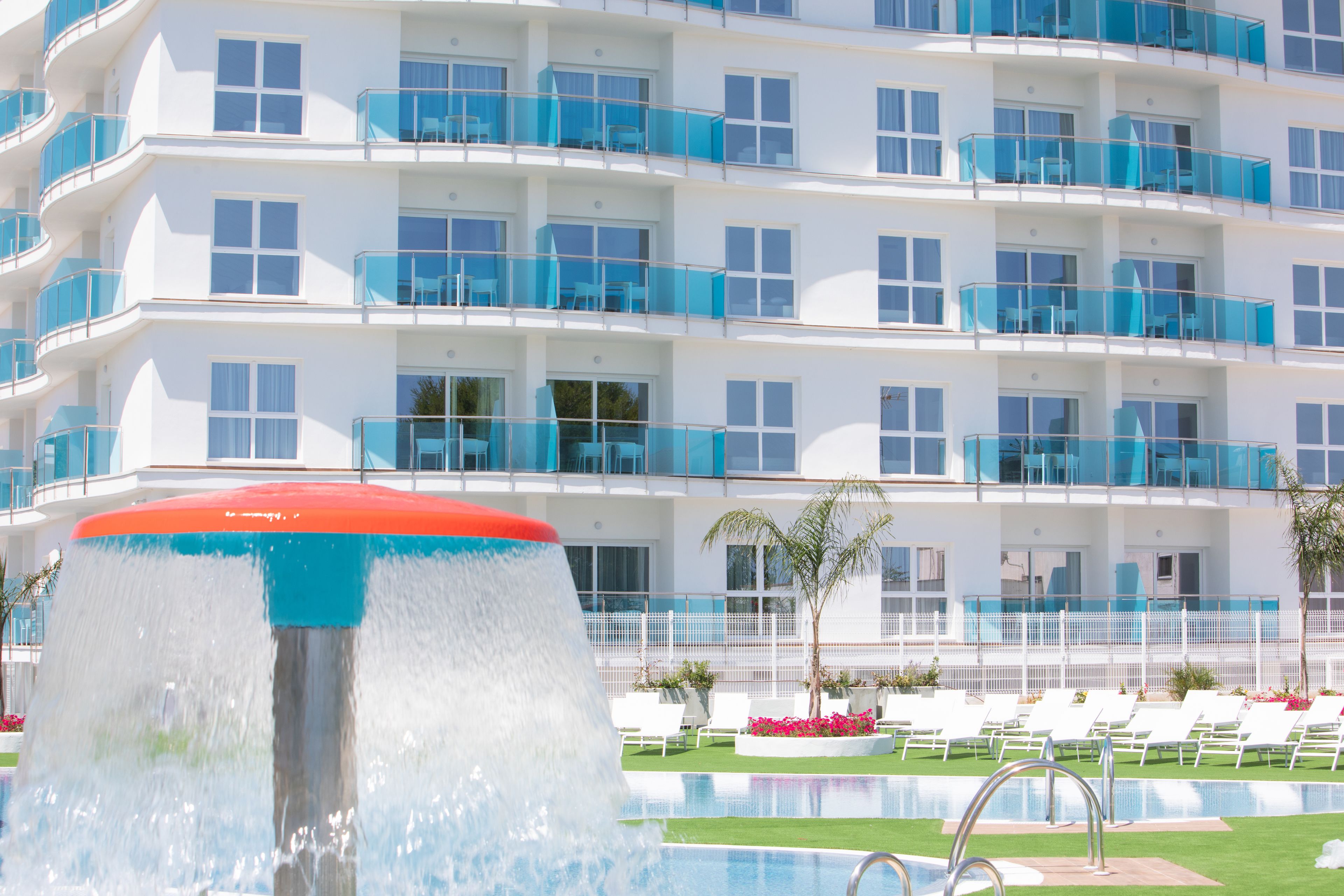 A hotel with multiple balconies, a swimming pool, and lounge chairs.