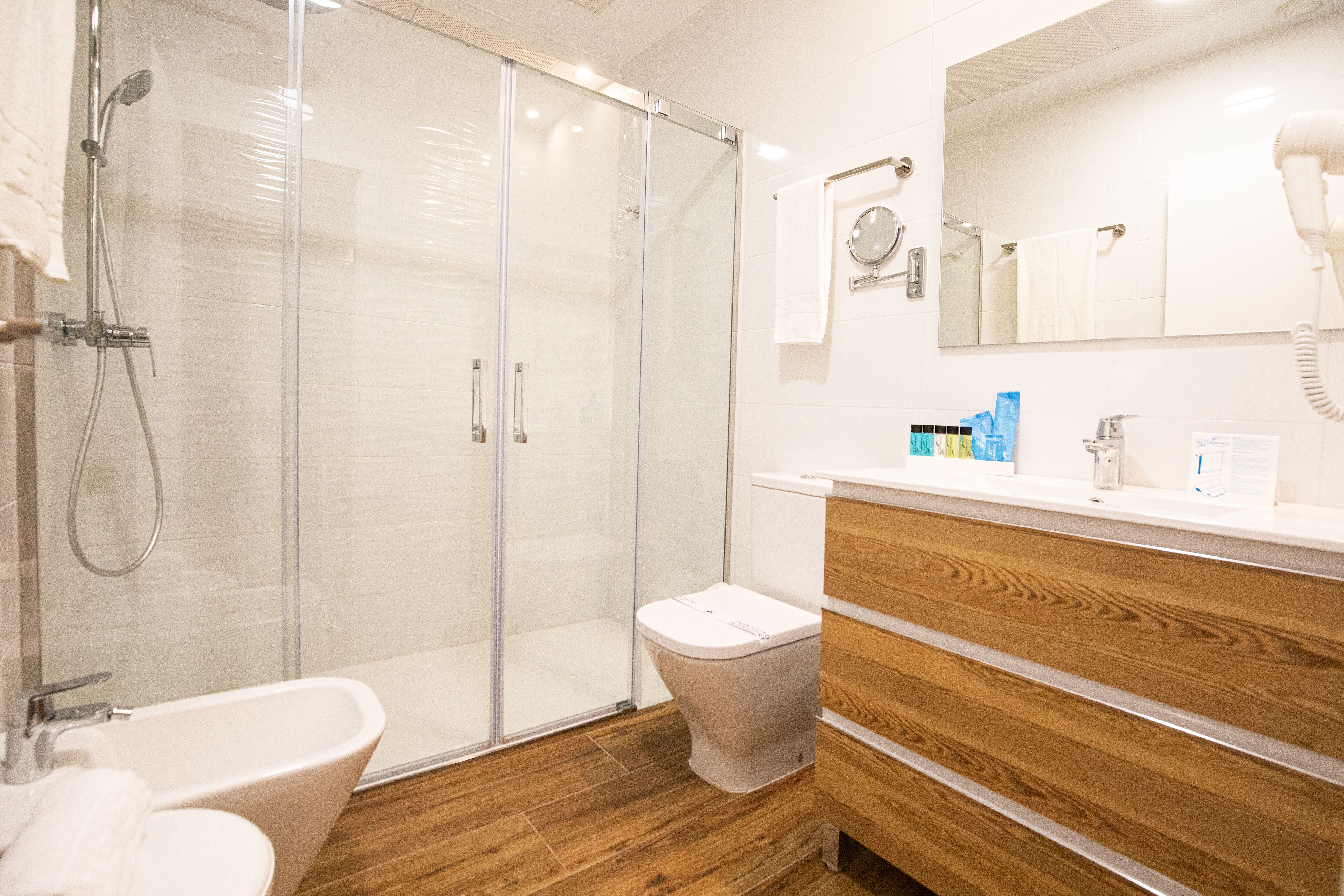 Un baño moderno con cabina de ducha de vidrio, tocador de madera y lavabo blanco.
