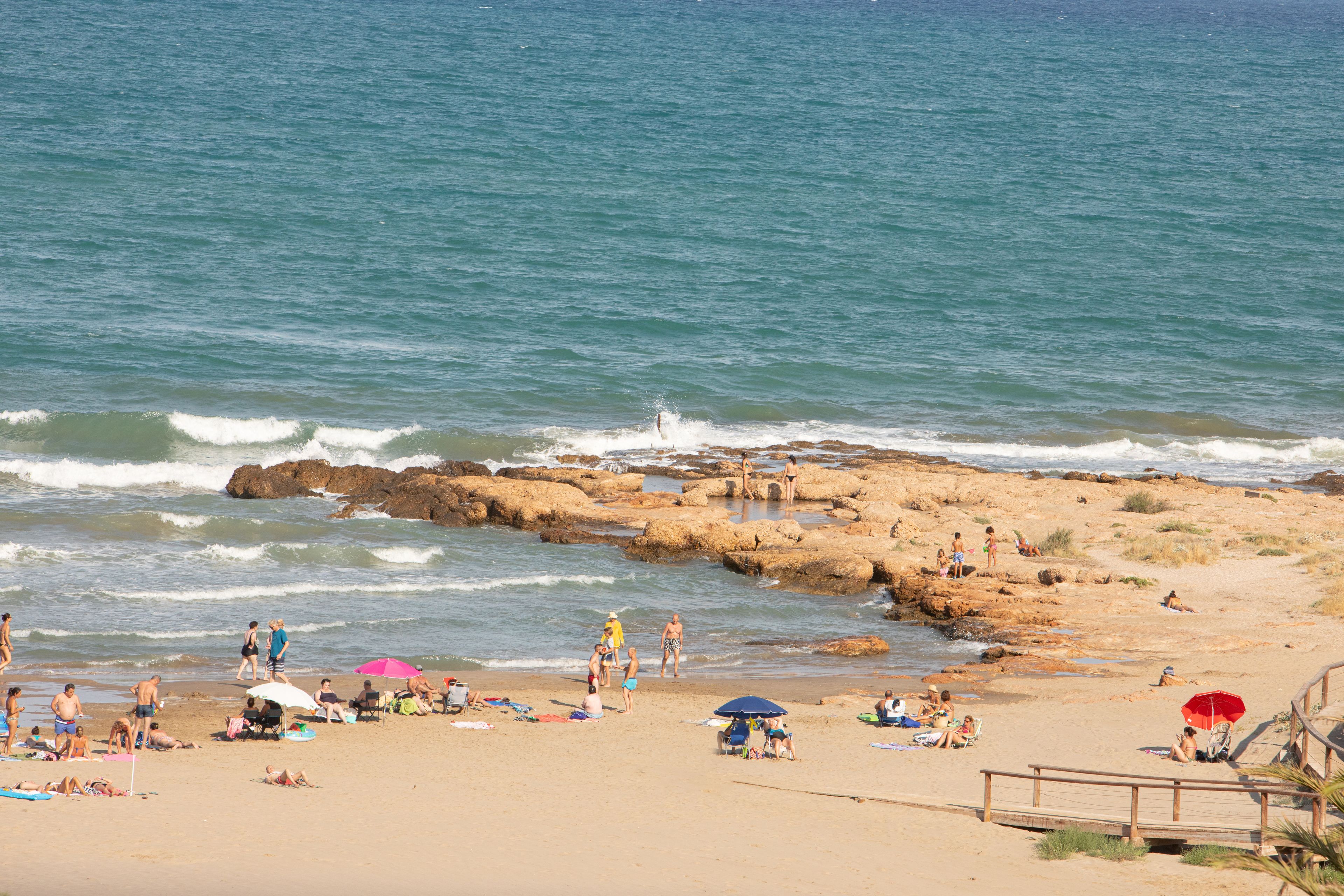 A beach with rocky formations, people sunbathing, and umbrellas.