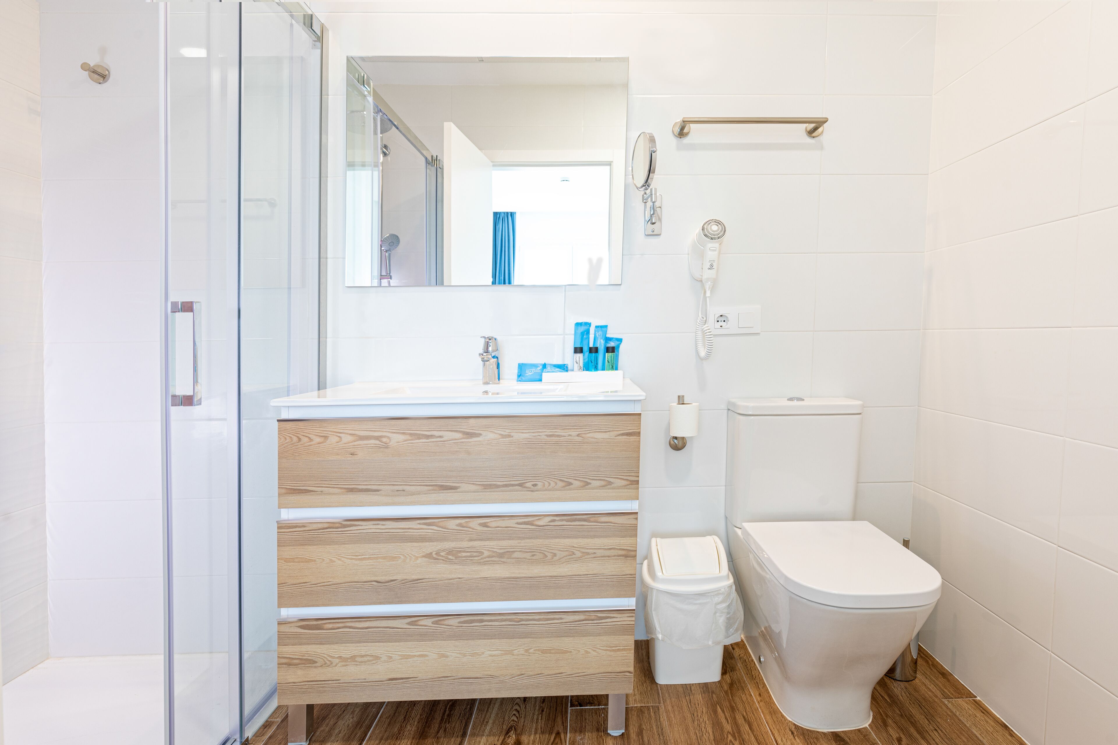 A modern bathroom with a glass shower enclosure, a wooden vanity, a toilet, and a mirror.