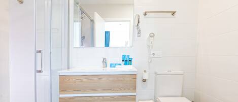 Un baño moderno con cabina de ducha de vidrio, tocador de madera, inodoro y espejo.