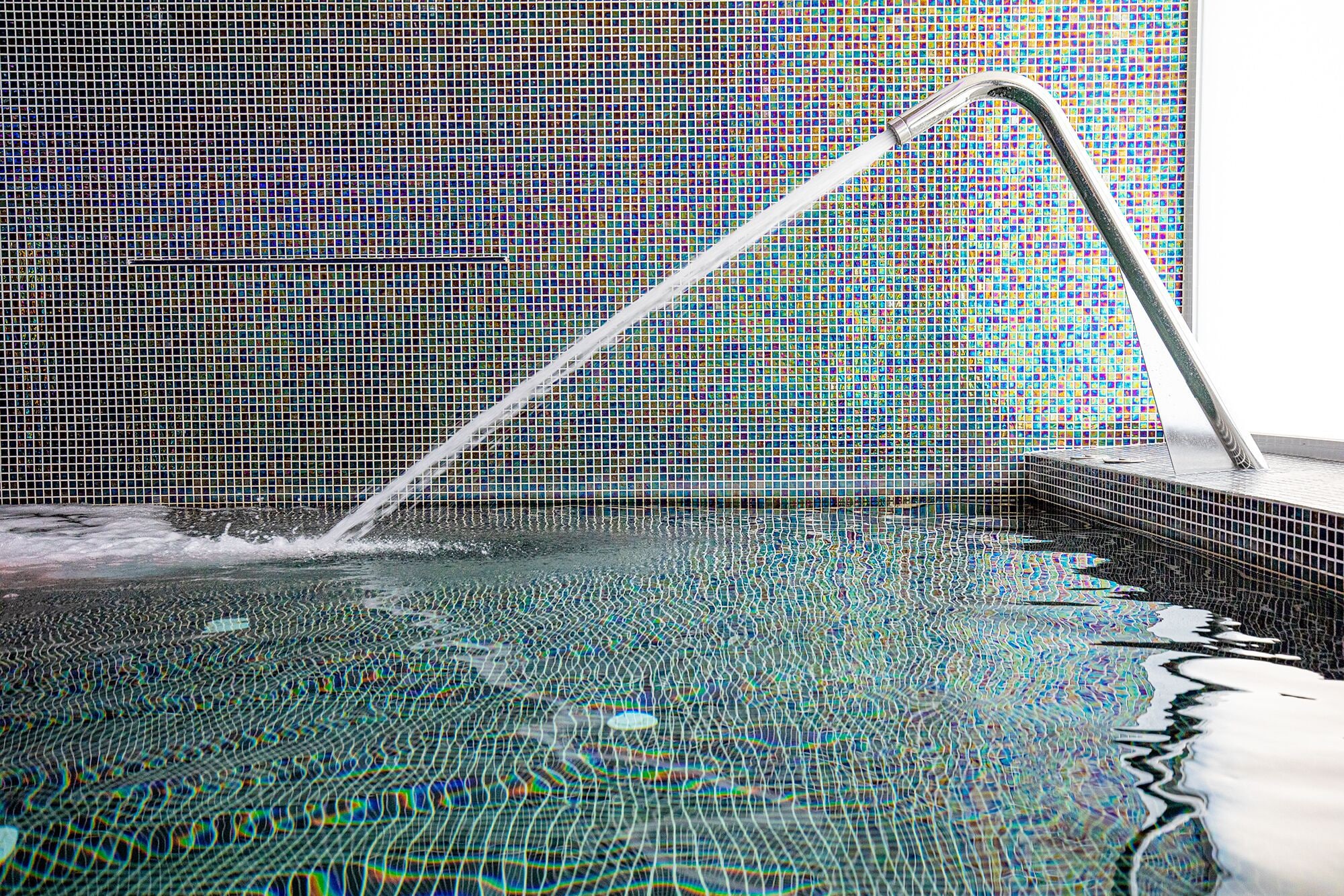 A swimming pool with a tiled wall and a metal faucet.