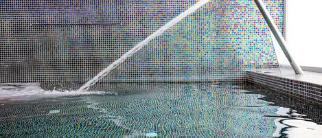 Une piscine avec un mur carrelé et un robinet en métal.