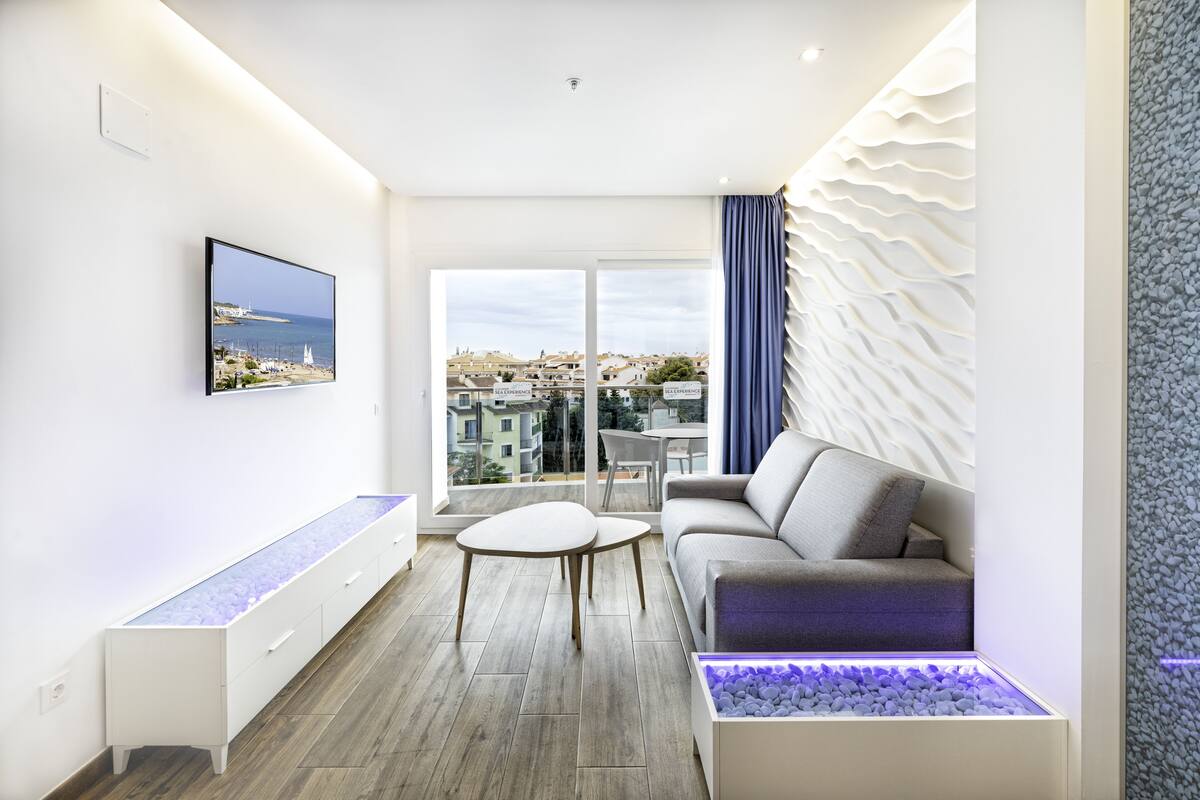 Una sala de estar moderna con un sofá, una mesa de centro, un televisor y vistas a la ciudad a través de grandes ventanales.
